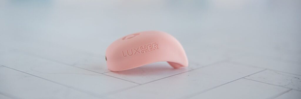 The LuxHer vibrator sits on a flat surface. The tip of the vibrator protrudes more than the flat surface of it, with a curvature designed to help wrap around the clitoris. For my Luxus review.