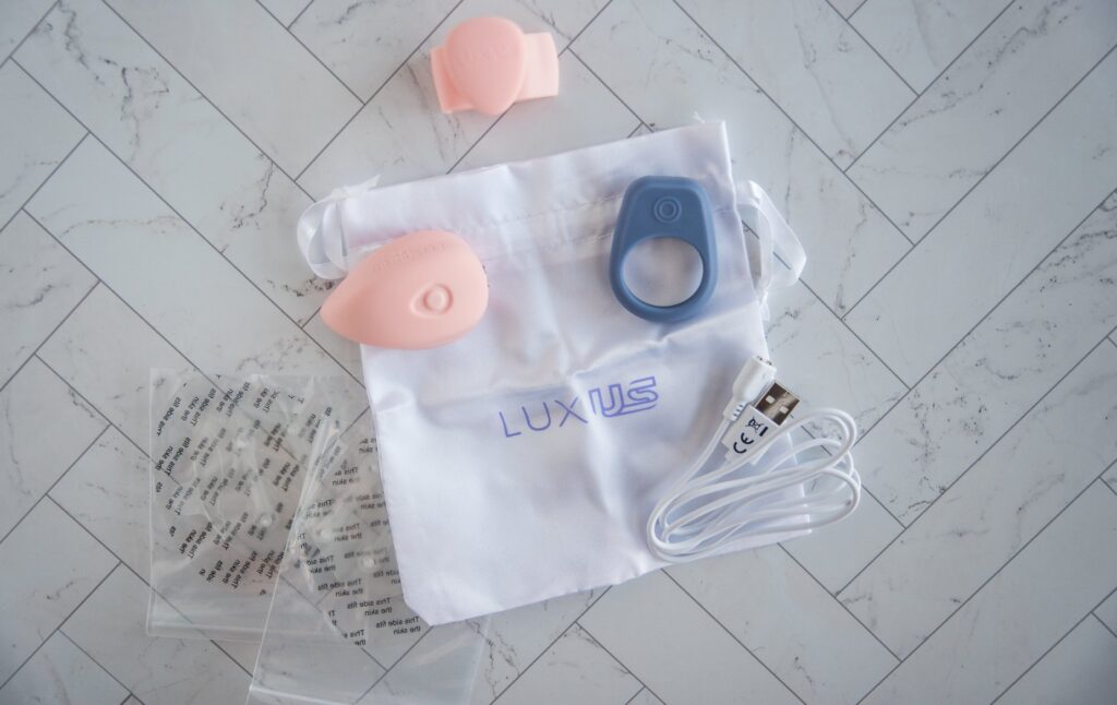 The Luxus set shown with everything included in it. There's the LuxHer and LuxHim, the Finger Grip, 2 Adhesive Stickers, a charging cable, and a white drawstring storage bag. For my Luxus review.