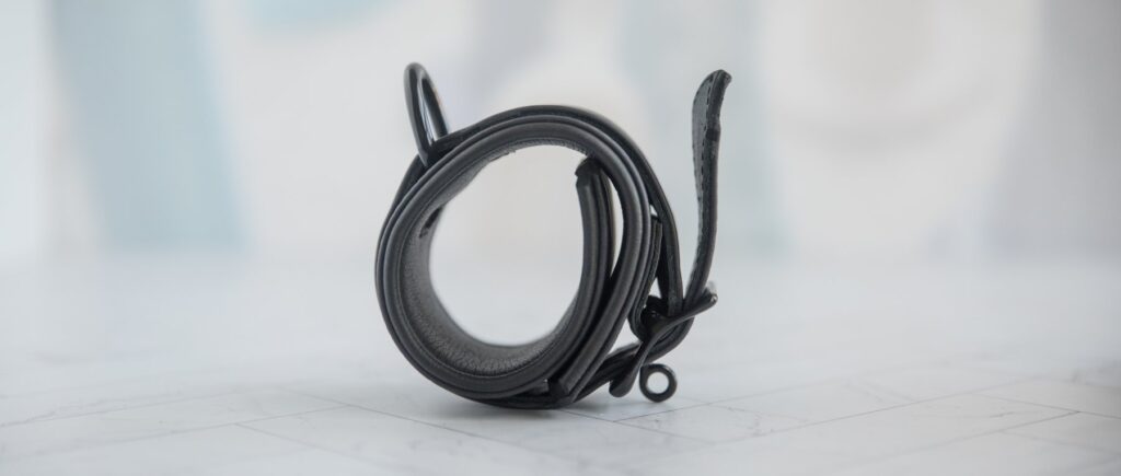 Side view of the neoprene bondage cuffs. The cuff has a single D-ring. It doesn't have an excess strap keeper, and the "tail" of the fastened strap is hanging loose. There's a circular fastening buckle where locks can be inserted. For my MEO.de Lockable Chicago Neoprene Restraints review.