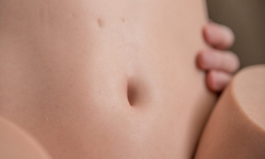 Close-up on the belly button of the love doll, showcasing the skin texturing of the doll. It looks like real human skin.