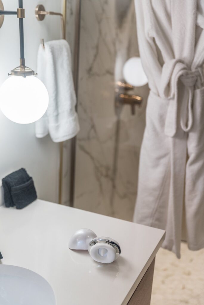 The Joylume Cloud Kiss sits out on a bathroom countertop. The shower is marbled in the background, and a robe hangs in the background.