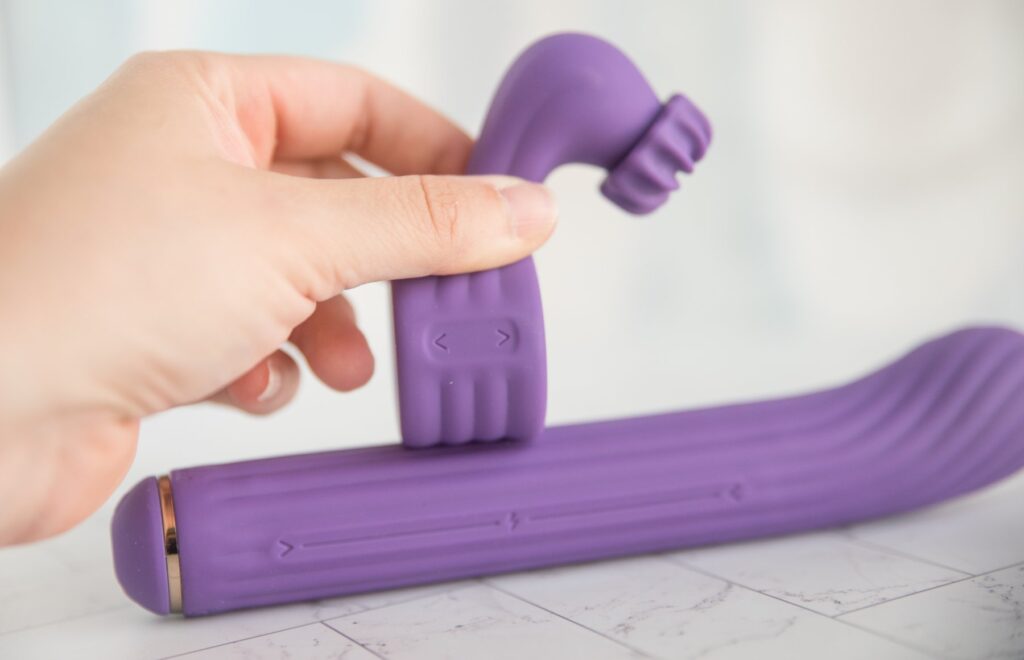My fingers hold the the clitoral attachment alongside the insertable shaft, showcasing how the two pieces work together and how the attachment can move alongside the powered track. For my AVIDLOVE PLAY Four-Attachment Rabbit Vibrator review.