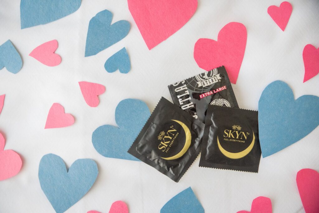 Three condoms are lying on top of white bedding. Little white and blue hearts are surrounding the condoms. For my article about what to do if you fall in love with your casual sex partner.