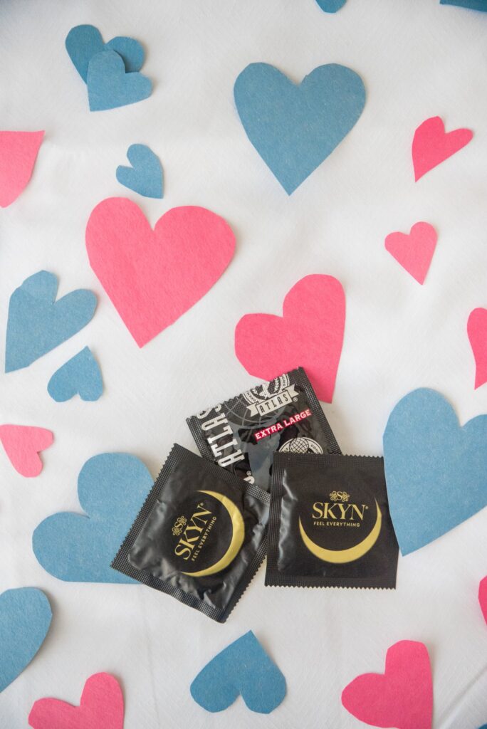 Three condoms are lying on top of white bedding. Little white and blue hearts are surrounding the condoms. For my article about what to do if you fall in love with your casual play partner.
