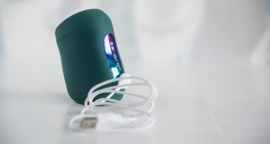 The magnetic charging cord shown adhered to the magnetic charging port area of the vibrator. The other end of the charging cable has a USB.