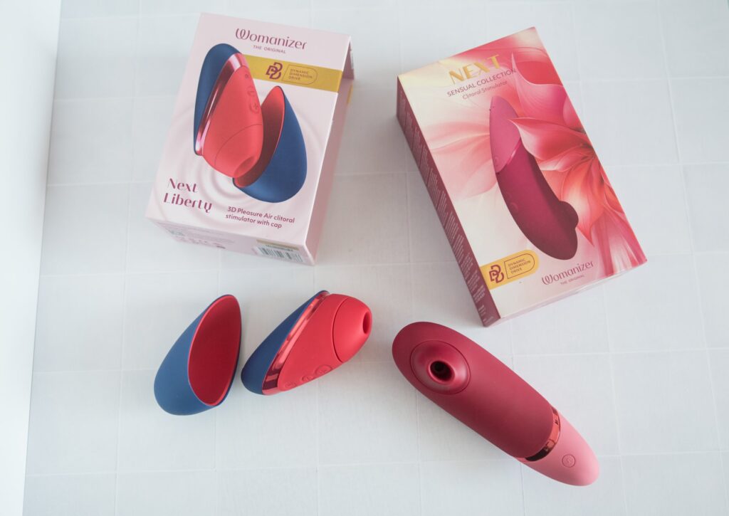 Both of the toys sit out, uncovered, next to one another and their packaging. For my Womanizer Next Liberty vs Womanizer Next comparison