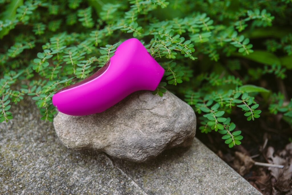 The toy sits on top of a rock with bright greenery in the background. For my AVIDLOVE PLAY Ergonomic Max Suction Clitoral vibrator review.