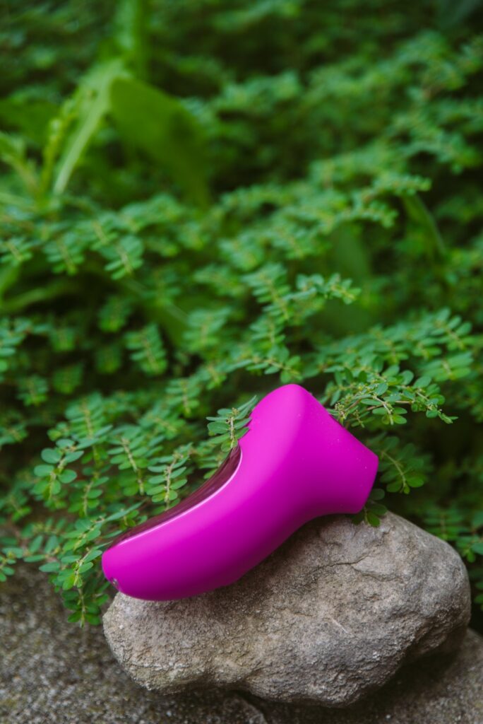 The toy sits on top of a rock with bright greenery in the background. For my AVIDLOVE PLAY Ergonomic Max Suction Clitoral vibrator review.
