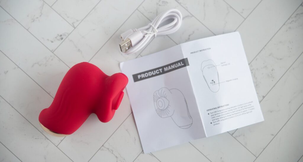 Everything included with the vibrator from a top-down view. There's the toy itself, the charging cable, and a single sheet instruction page. For my AVIDLOVE PLAY Kiss Air Pulse Vibrator Review.