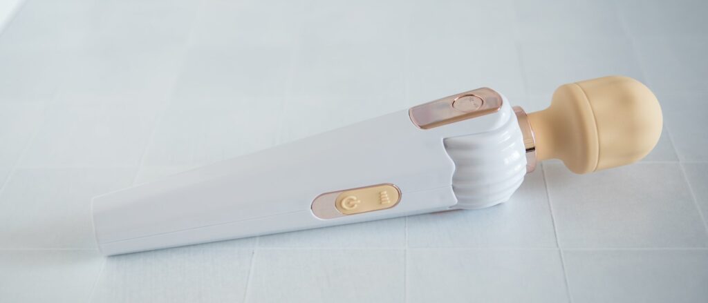 The wand massager is laid straight out and resting on its side. There are two clearly marked buttons on the side. The massager looks very straightforward.