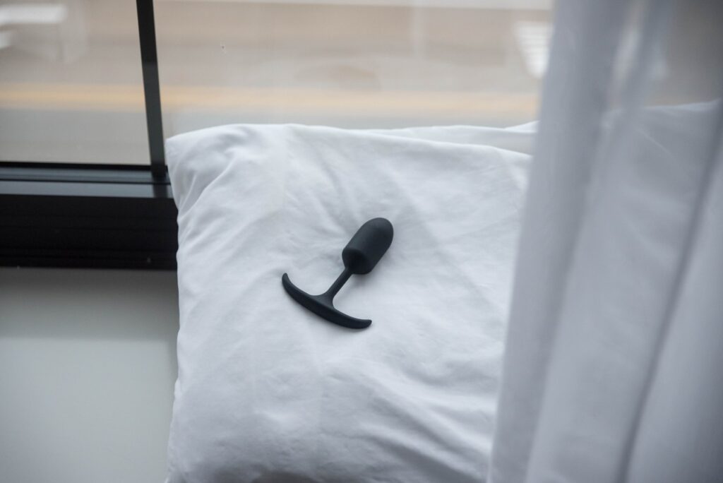 The Booty Buddy plug lies out on top of a plain white pillow near a reflective window. It looks bright, airy, and inviting. For my MEO.de Booty Buddy review.